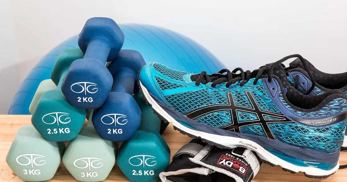 Halteres coloridos, bola de pilates e tênis azul de corrida sobre uma mesa