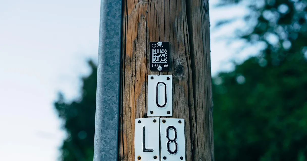 Etiqueta com QR Code fixada em um poste de madeira ao lado de placas numeradas